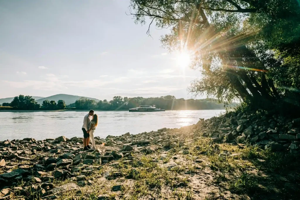 A couple enjoying a romantic moment on a rocky riverside at sunset.