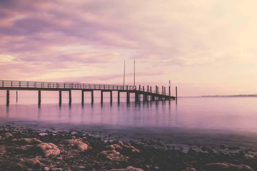 A tranquil sunset over a pier in Konstanz, Germany with soft pink hues reflecting on the water.