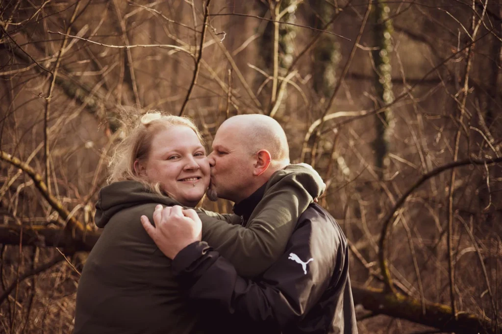 A joyful couple embracing and sharing a tender moment in a scenic forest area.