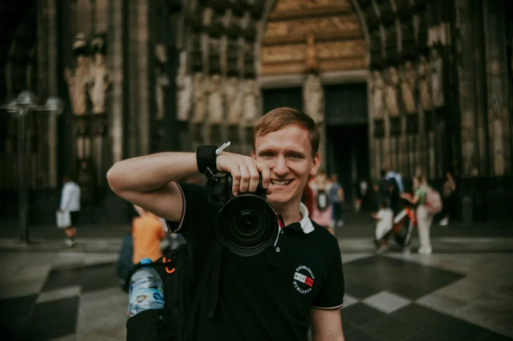 A photographer smiling with camera in front of a historical cathedral entrance.