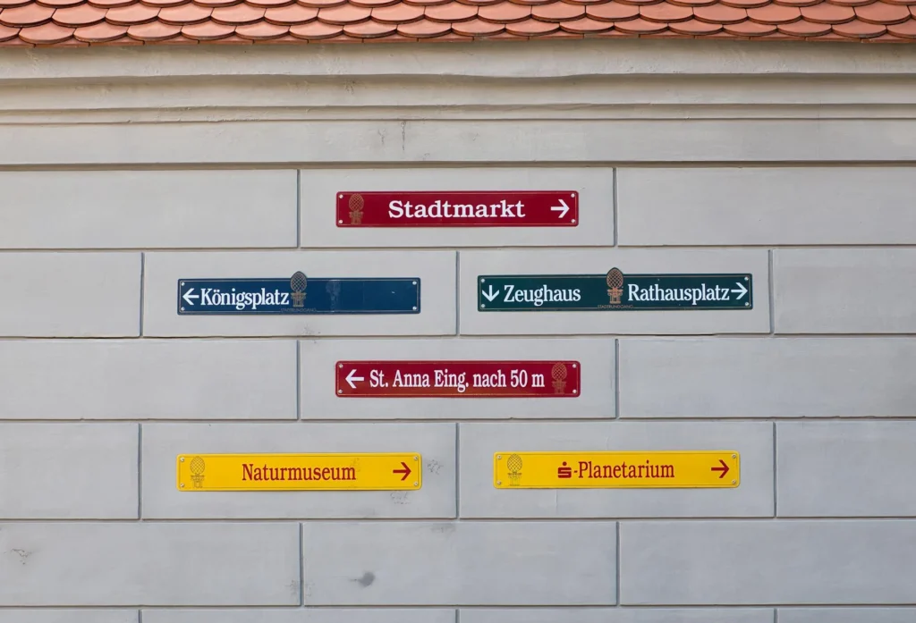 Vibrant directional signs on a wall in Augsburg guide visitors to local attractions like Stadtmarkt and Planetarium.