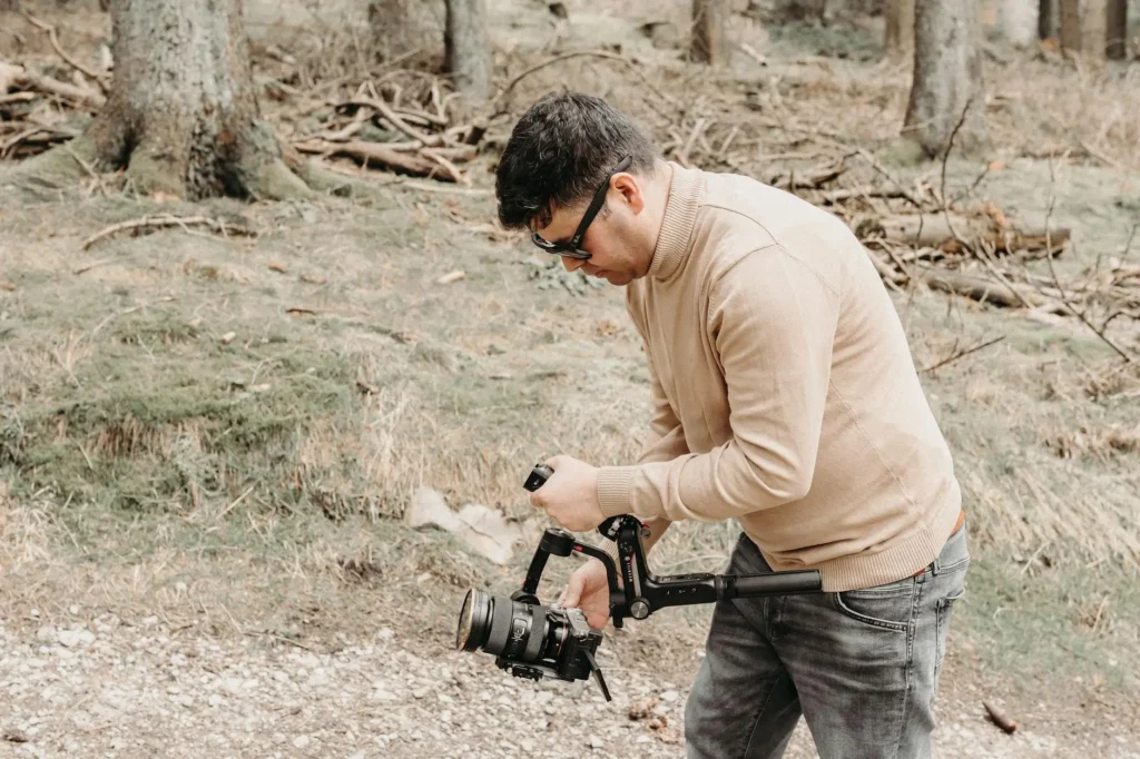 A male photographer operates a camera stabilizer during a film shoot in a forest.
