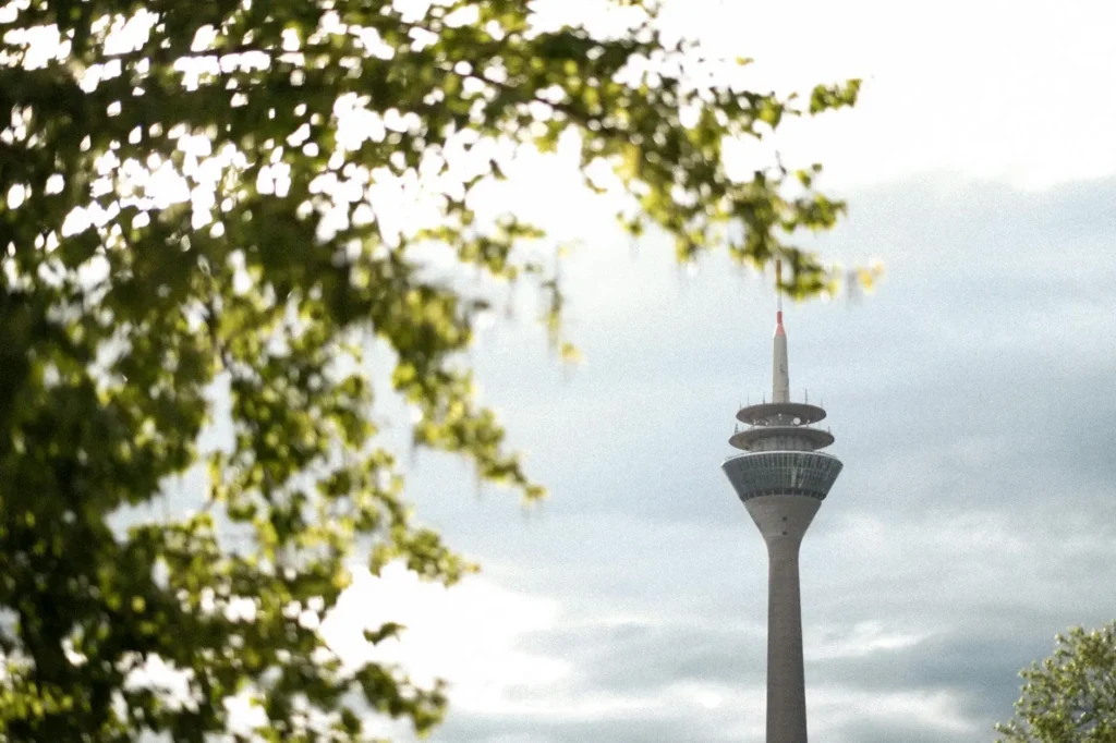 View of the iconic Rheinturm tower framed by lush green trees in Düsseldorf, Germany.