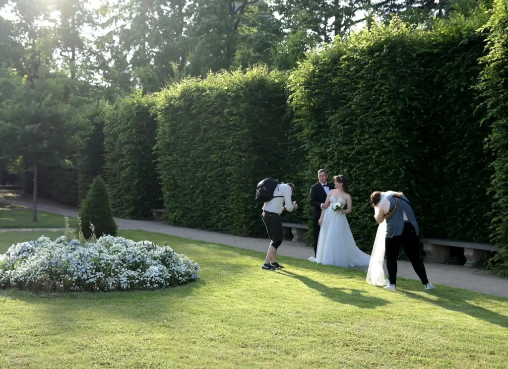 Bride and groom pose for photographers in a lush garden during sunny day.