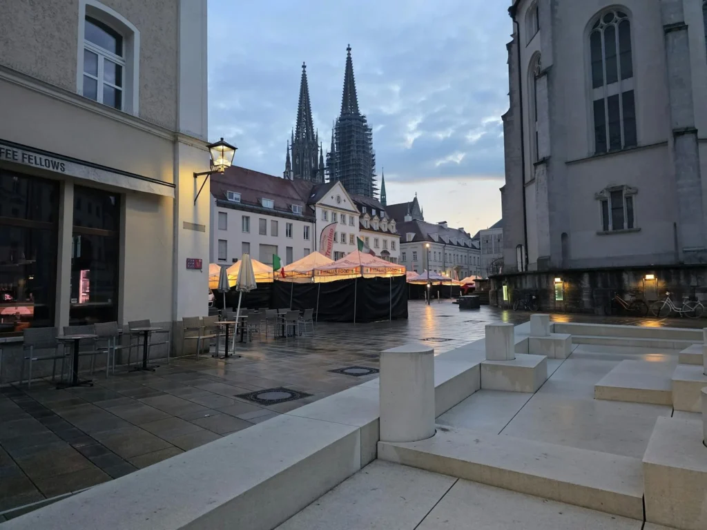 Twilight view of Regensburg Cathedral, Germany with street architecture and empty outdoor seating.