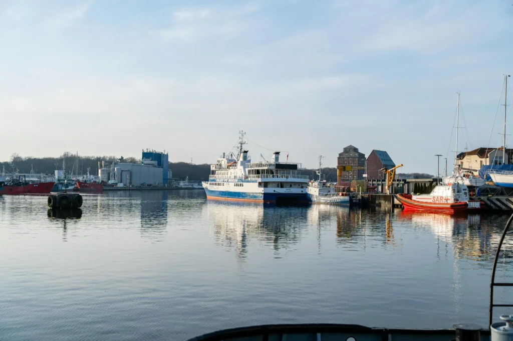 Peaceful harbor scene in Kołobrzeg, Poland, featuring boats and reflections on a calm day.