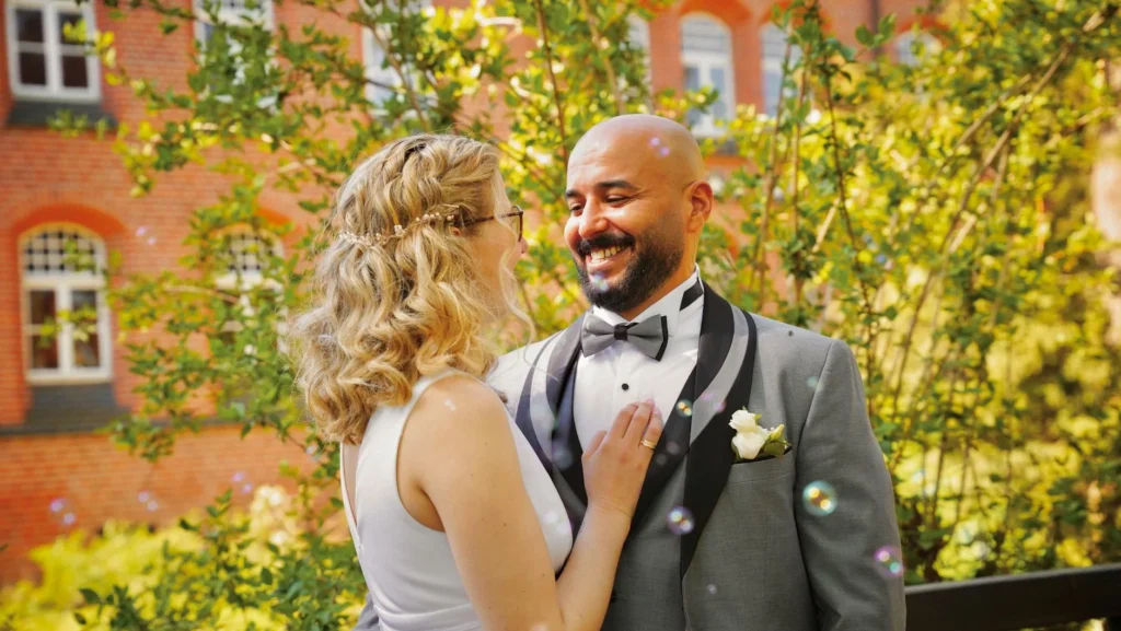 A joyful wedding couple embraces amidst a sunny garden setting in Hamburg, Germany.
