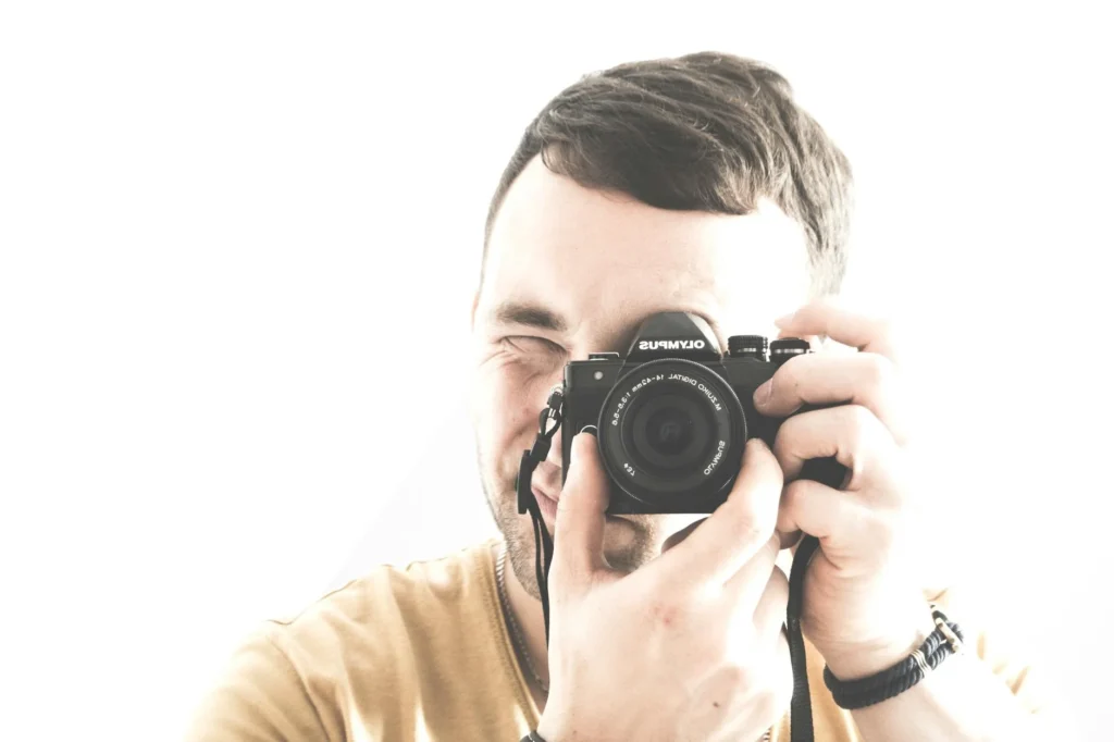 Candid portrait of a young male photographer capturing a shot in a bright studio setting.