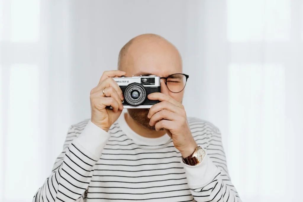 Bald man capturing a moment with a vintage camera indoors.
